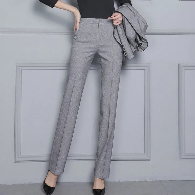 Person wearing gray pants with a gray jacket over the shoulder against a light gray wall.