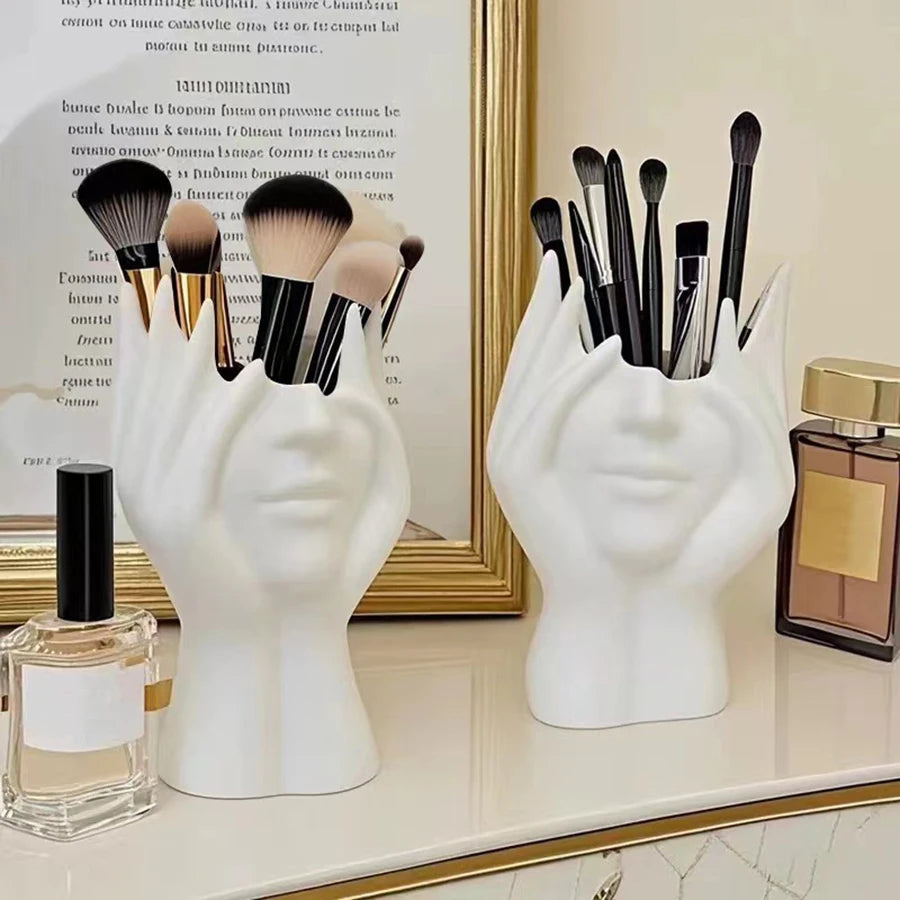 Two white hand-shaped brush holders with makeup brushes on a vanity.