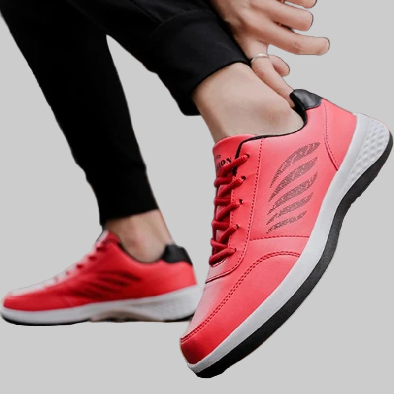 Red sneakers with black soles worn by a person sitting on a bench.