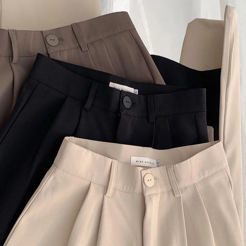 Three pairs of pants in black, beige, and brown on a white background