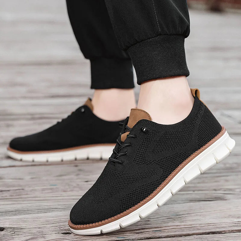 Black casual shoes with white soles worn by a person on a wooden floor.
