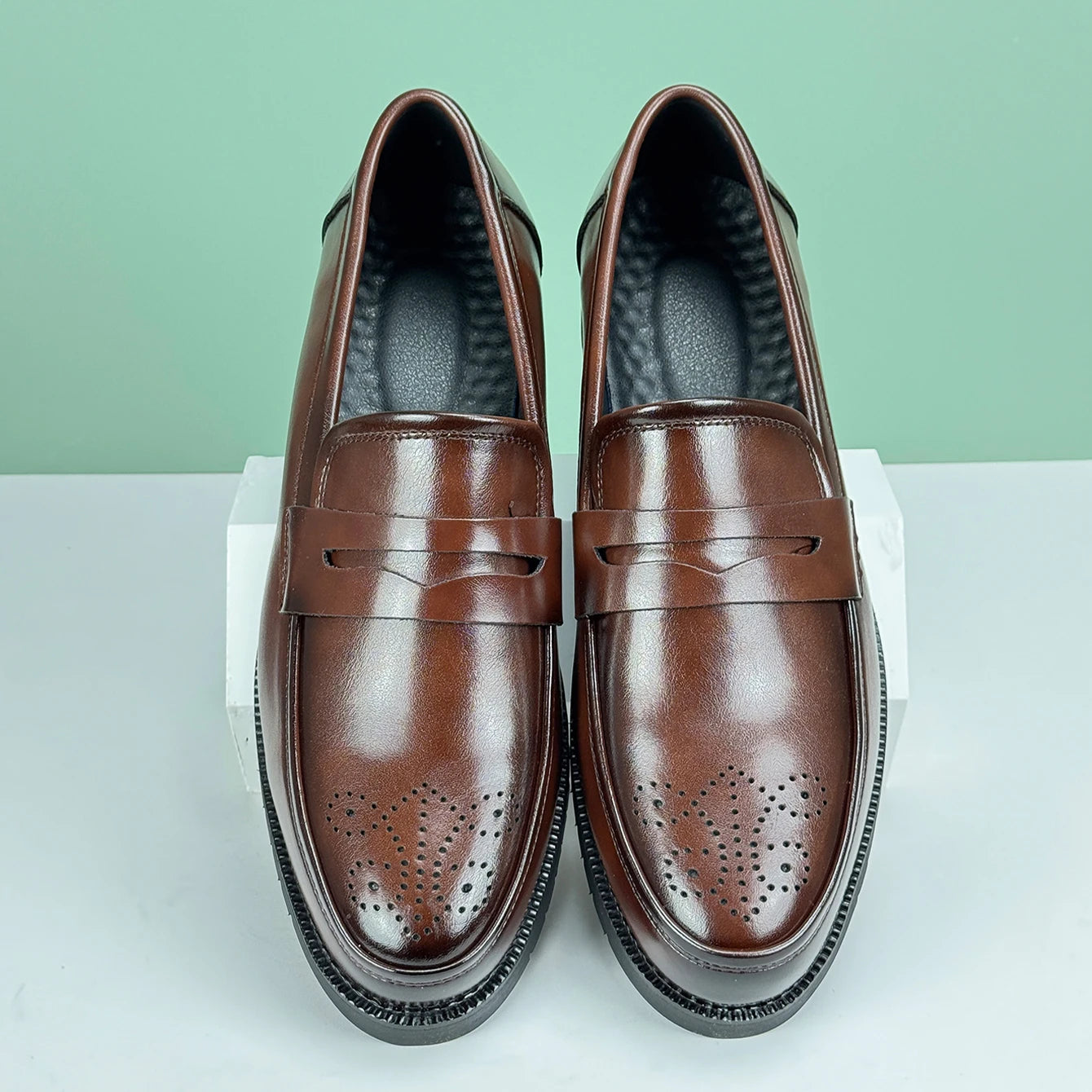 Pair of brown leather loafers on a white surface with a light green background