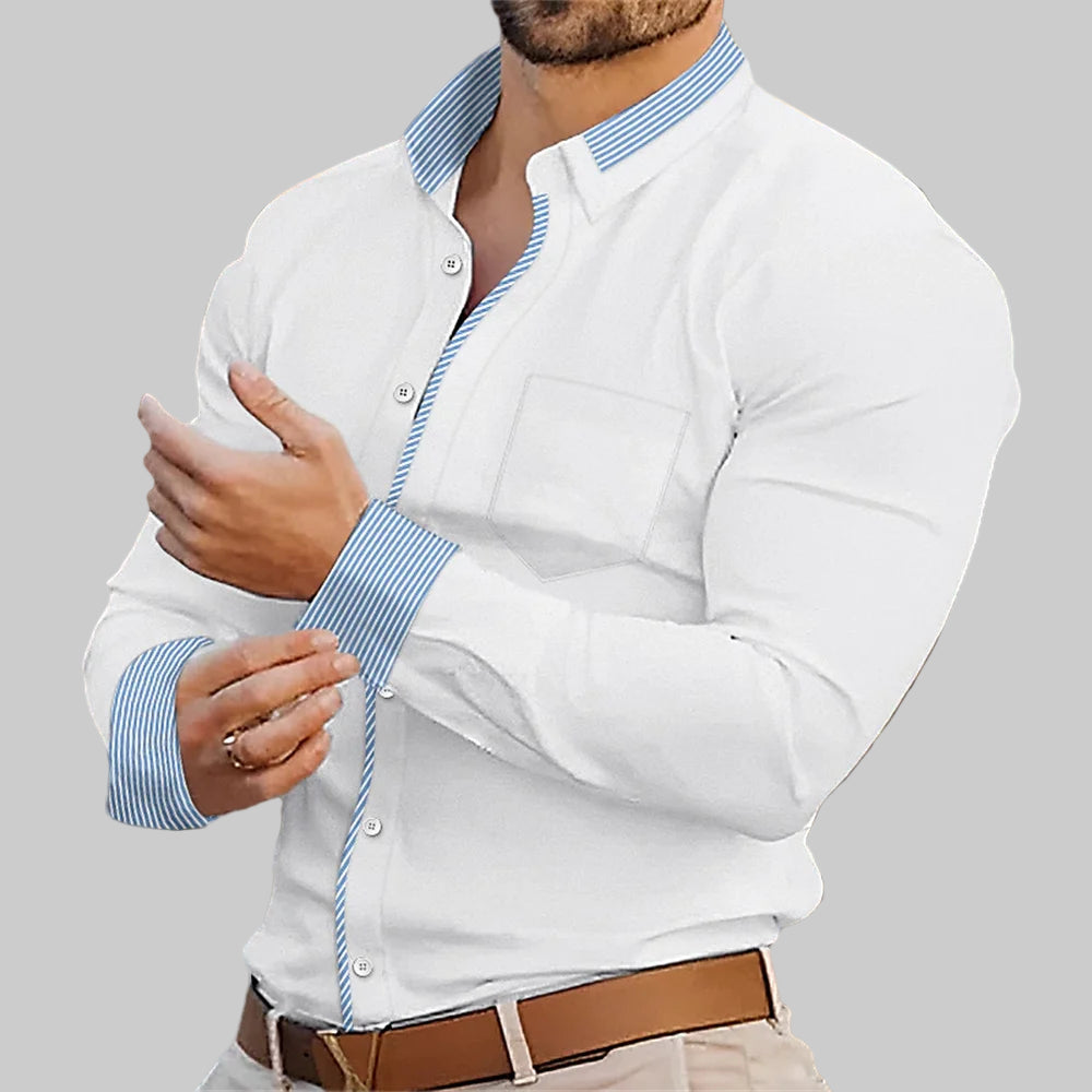Man wearing a white shirt with blue striped cuffs and a brown belt, standing in an outdoor setting.