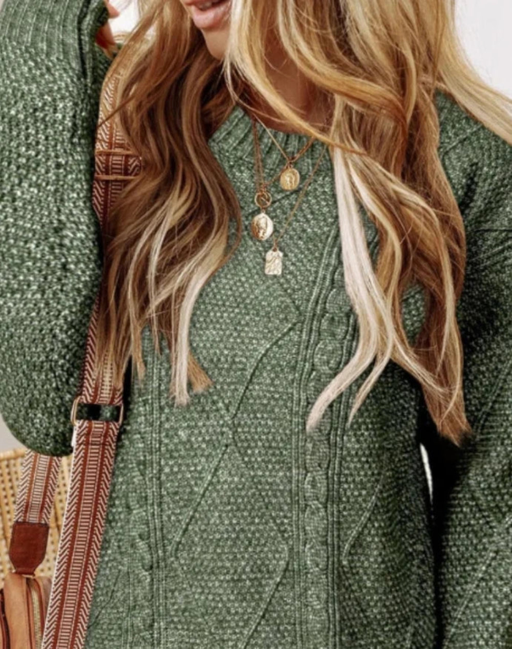 Person wearing a green textured coat with long blonde hair and a strap over shoulder.