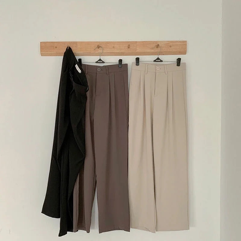 Three pairs of pants hanging on a wooden rack against a white wall.