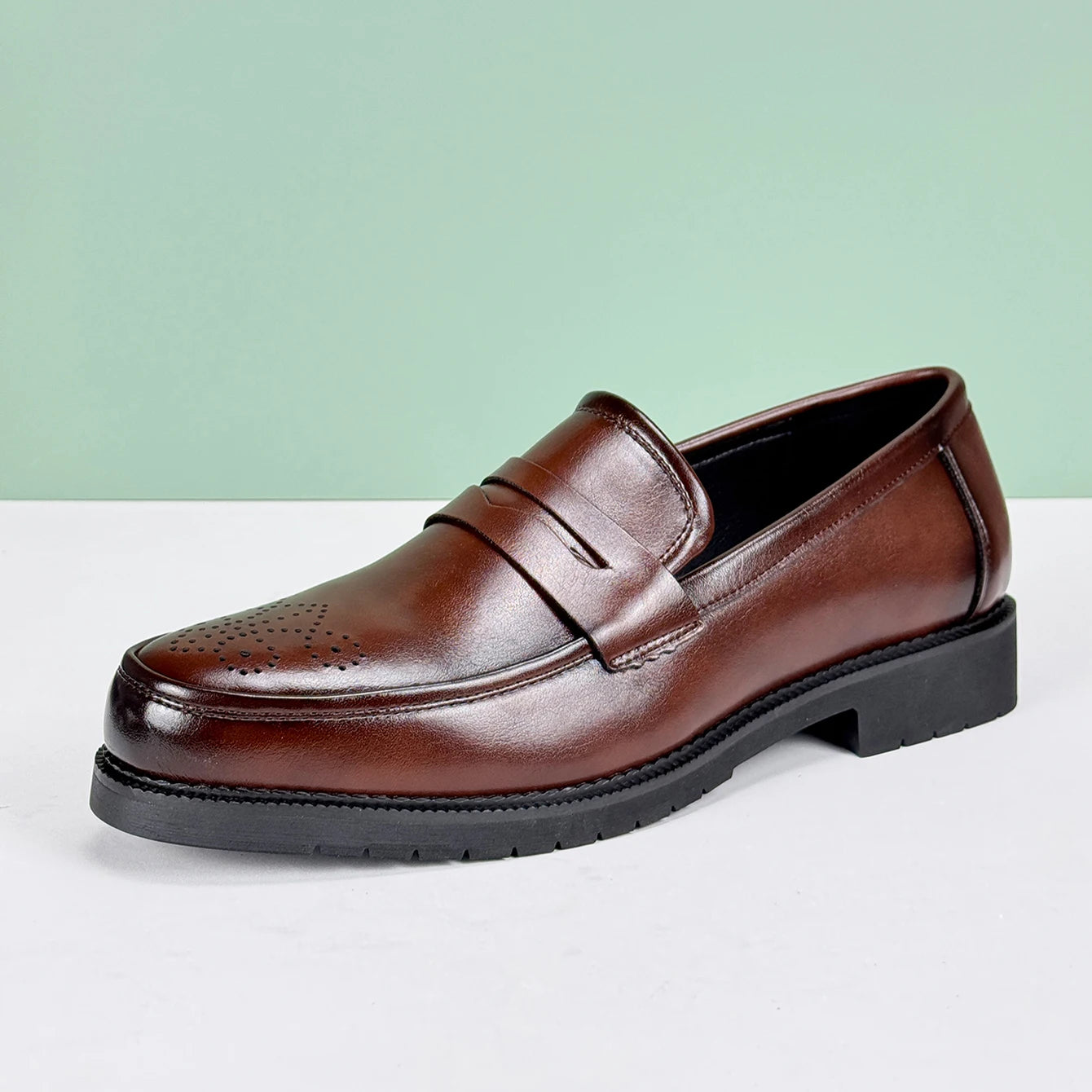 Brown leather loafer shoe on a light gray surface with a light green background