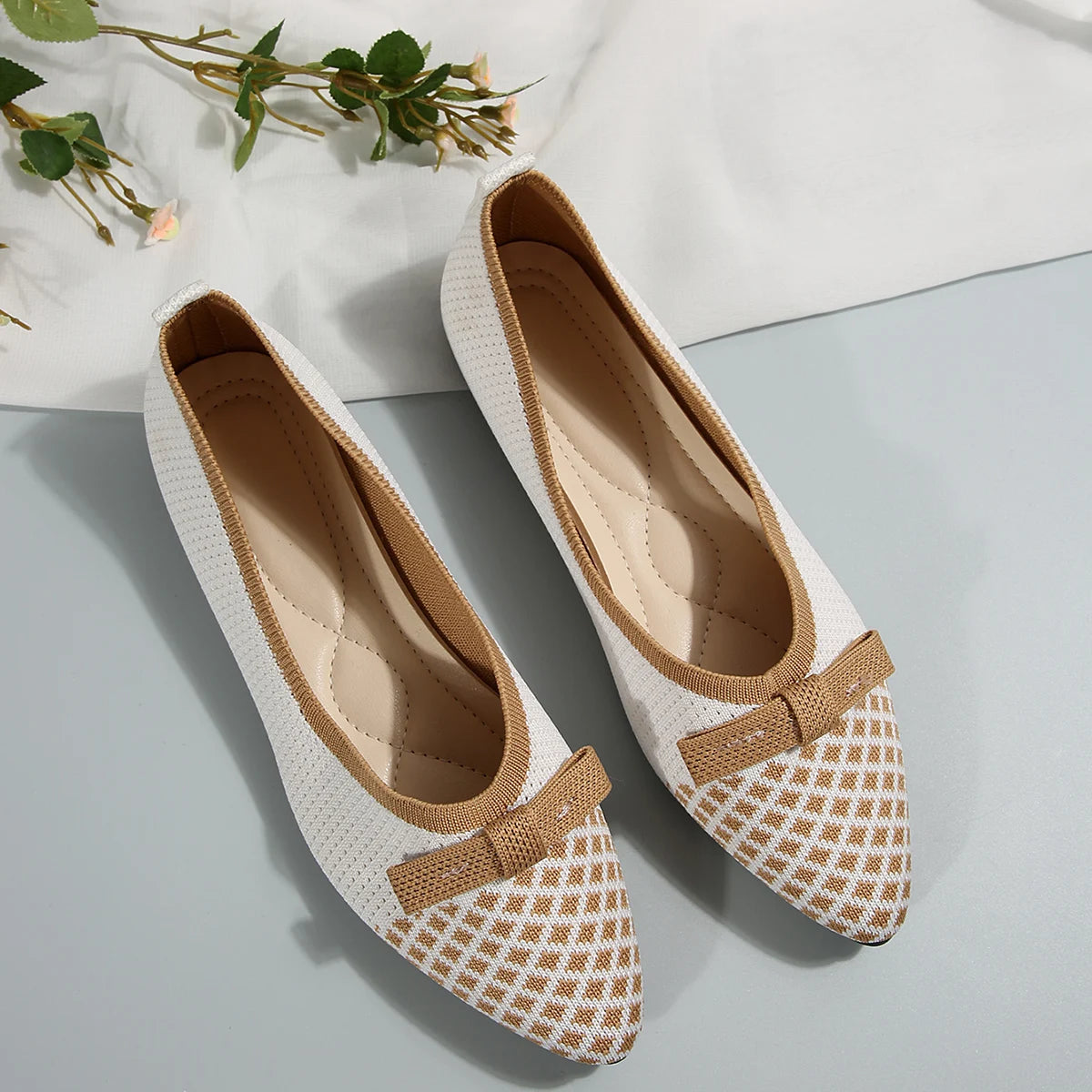Pair of white and brown checkered flats with a bow on a light gray surface.
