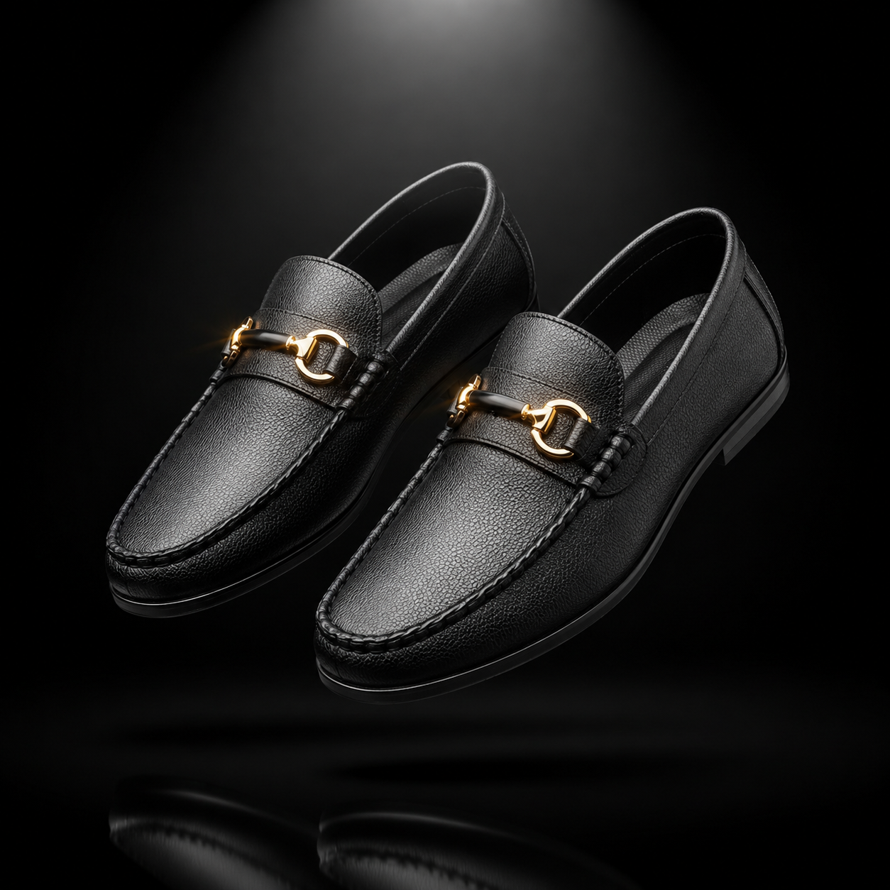 A pair of black leather penny loafers with gold-tone horsebit hardware, shown floating against a dark black background with a subtle reflection below.