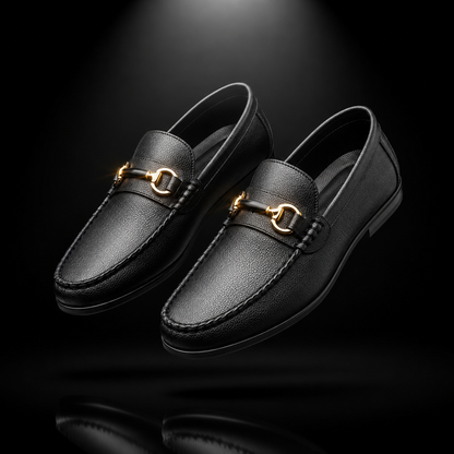 A pair of black leather penny loafers with gold-tone horsebit hardware, shown floating against a dark black background with a subtle reflection below.