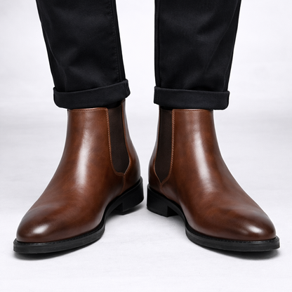 Brown leather Chelsea boots worn with black pants on a white background