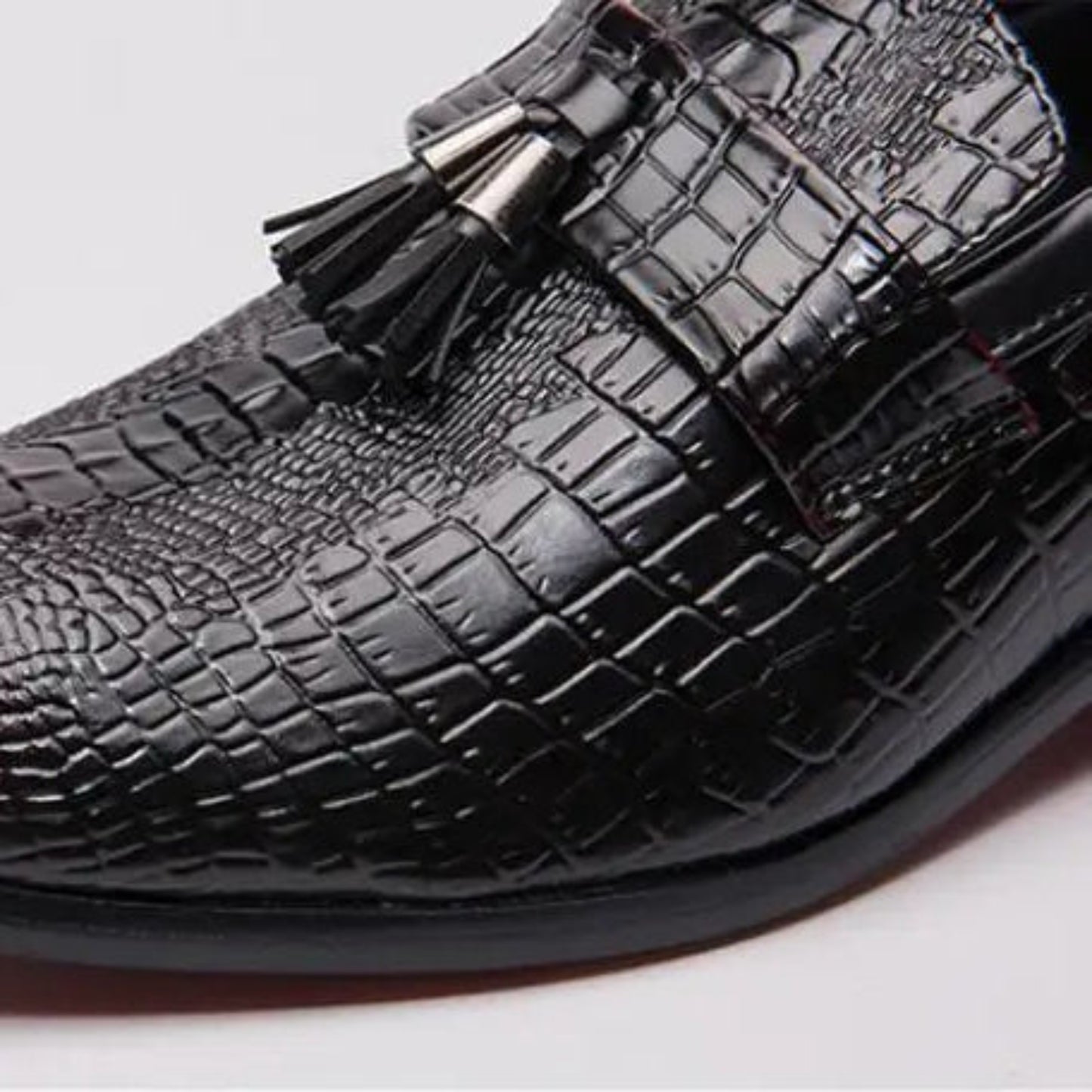 Black crocodile-patterned loafers with tassels on a light gray background