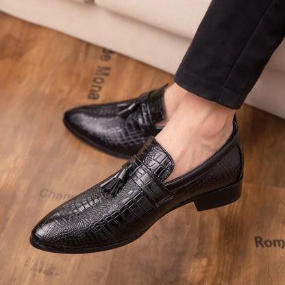 Black crocodile-patterned loafers worn on a wooden floor.