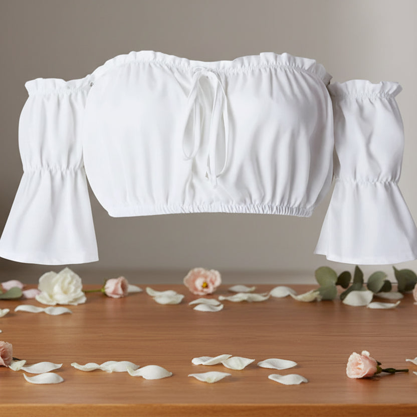 White off-shoulder top on a wooden surface with flower petals and greenery.