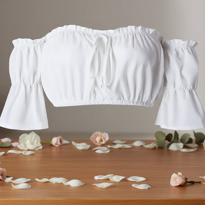 White off-shoulder top on a wooden surface with flower petals and greenery.