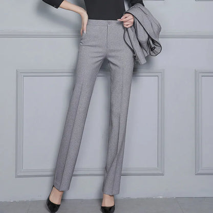 Person wearing gray pants with a gray jacket over the shoulder against a light gray wall.