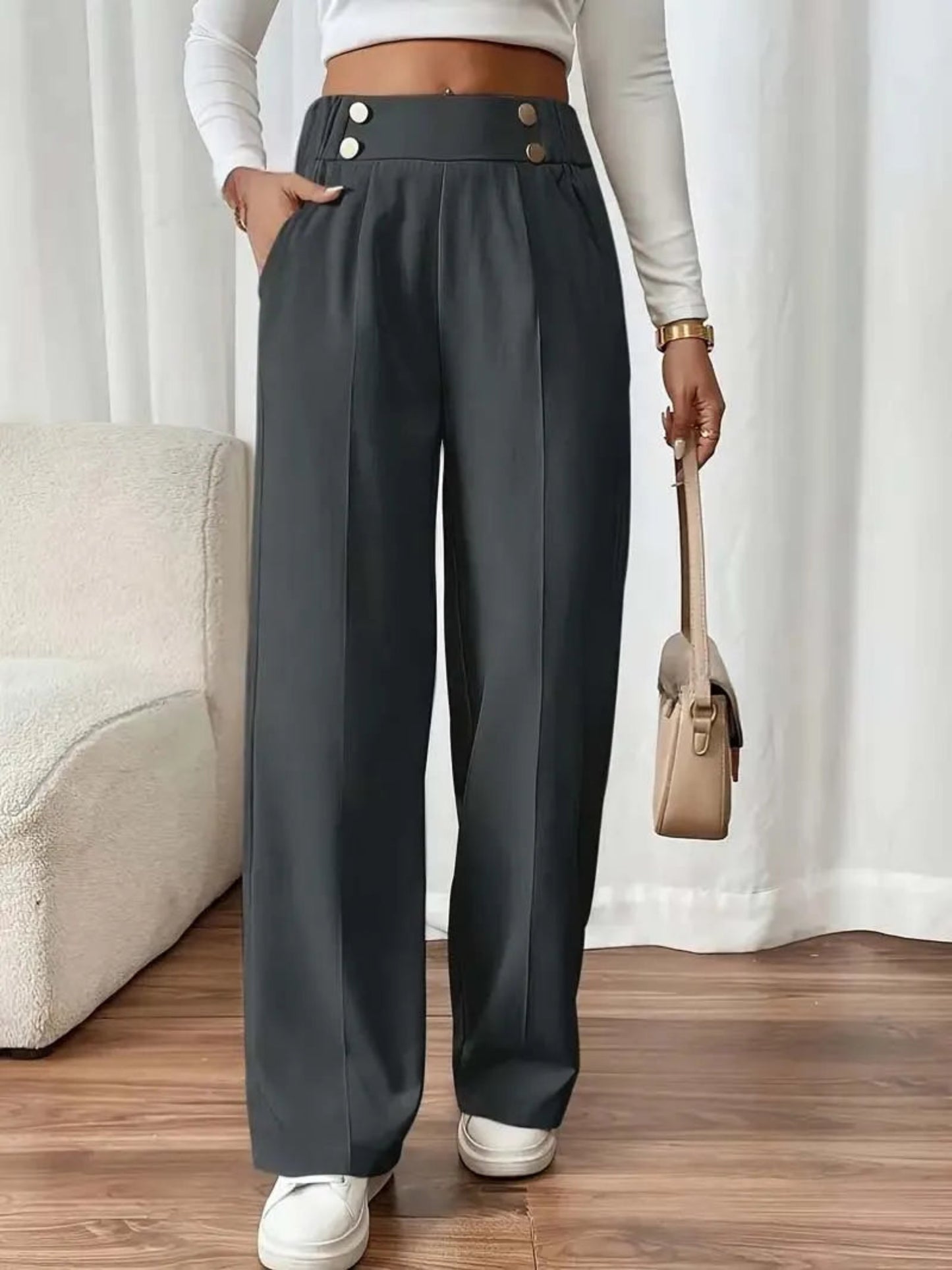 Person wearing dark gray wide-leg pants with a beige handbag indoors.