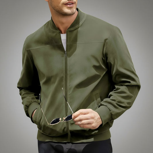 Man wearing a green bomber jacket holding sunglasses, standing next to a car.