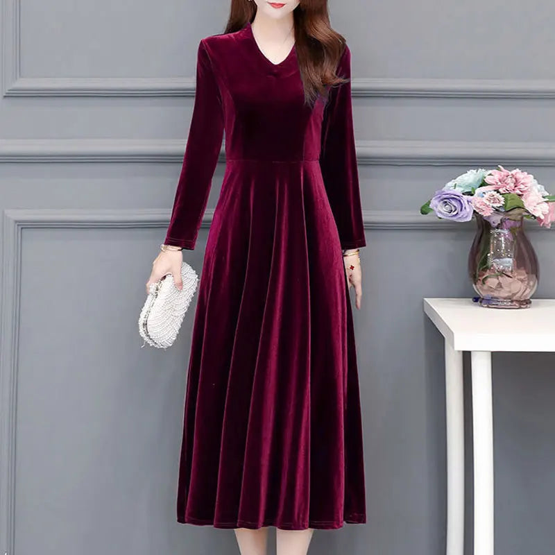 Woman wearing a burgundy velvet dress against a gray wall with a small table and flowers.