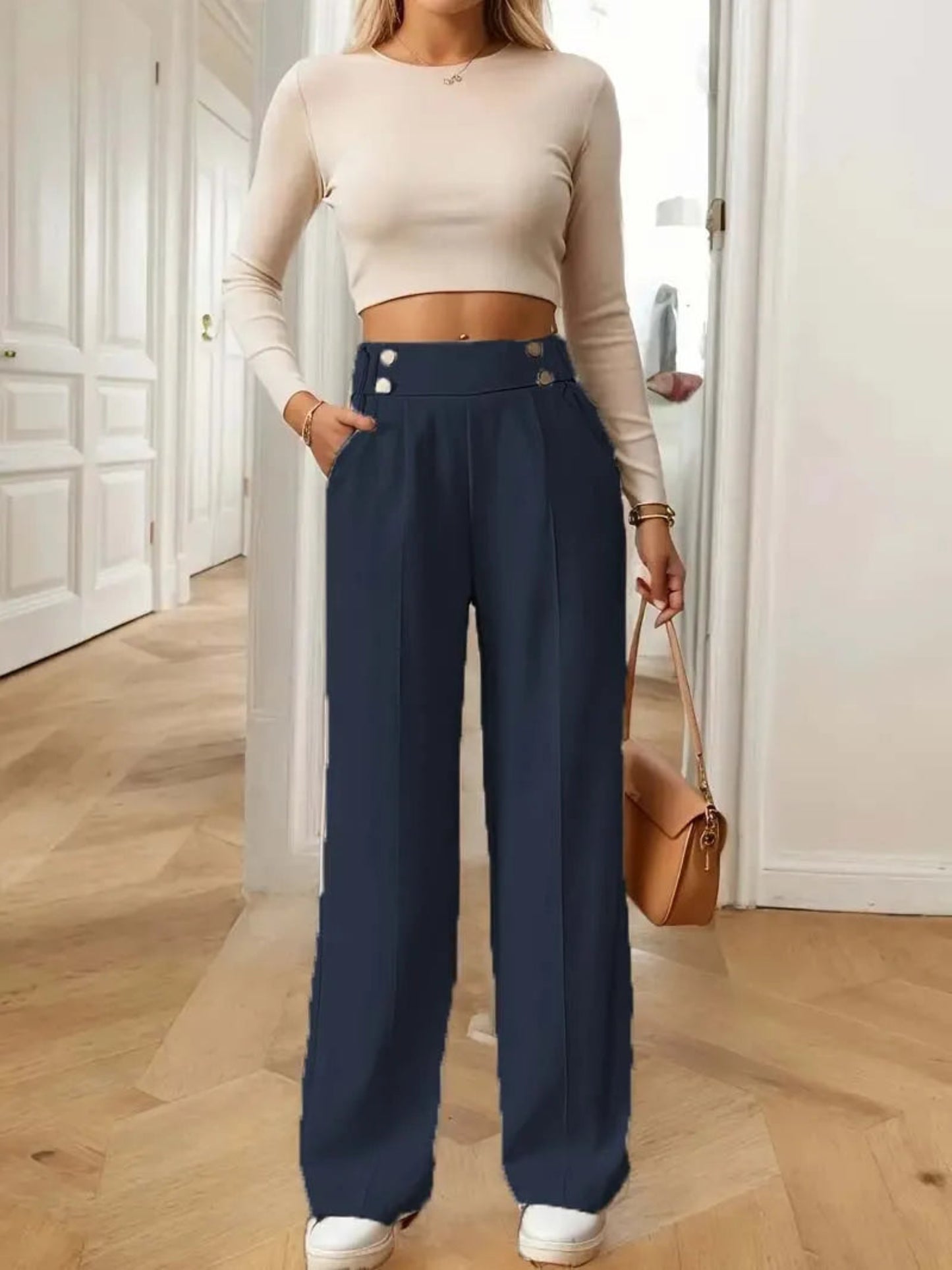 Person wearing a beige long-sleeve top and navy wide-leg pants, standing in a room with wooden flooring.