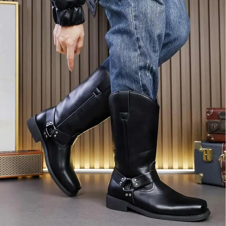 Person wearing black leather boots with buckles, standing against a neutral background.