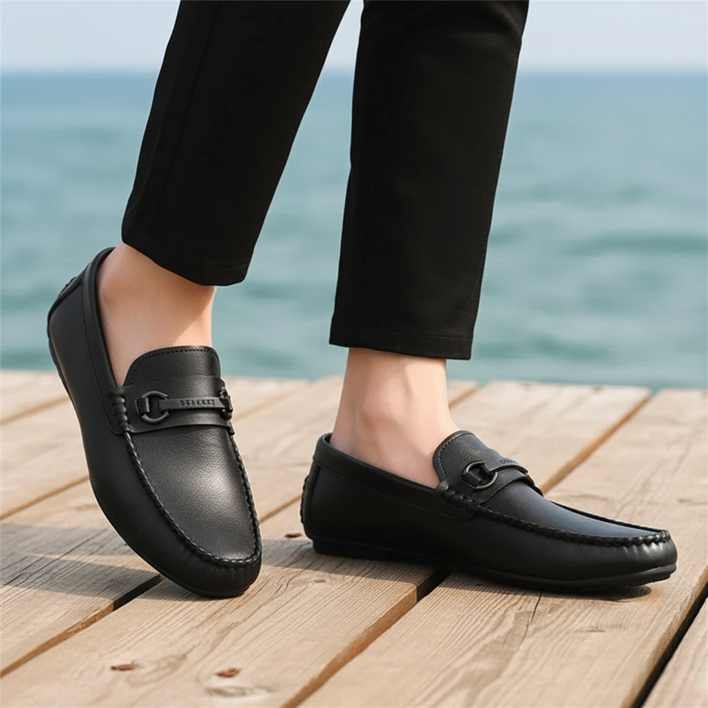 Black leather loafers worn with black pants on a neutral background