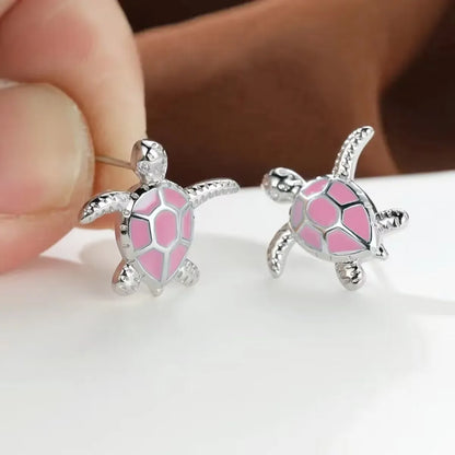 Tortoiseshell-shaped earrings with pink accents held by a hand on a white background