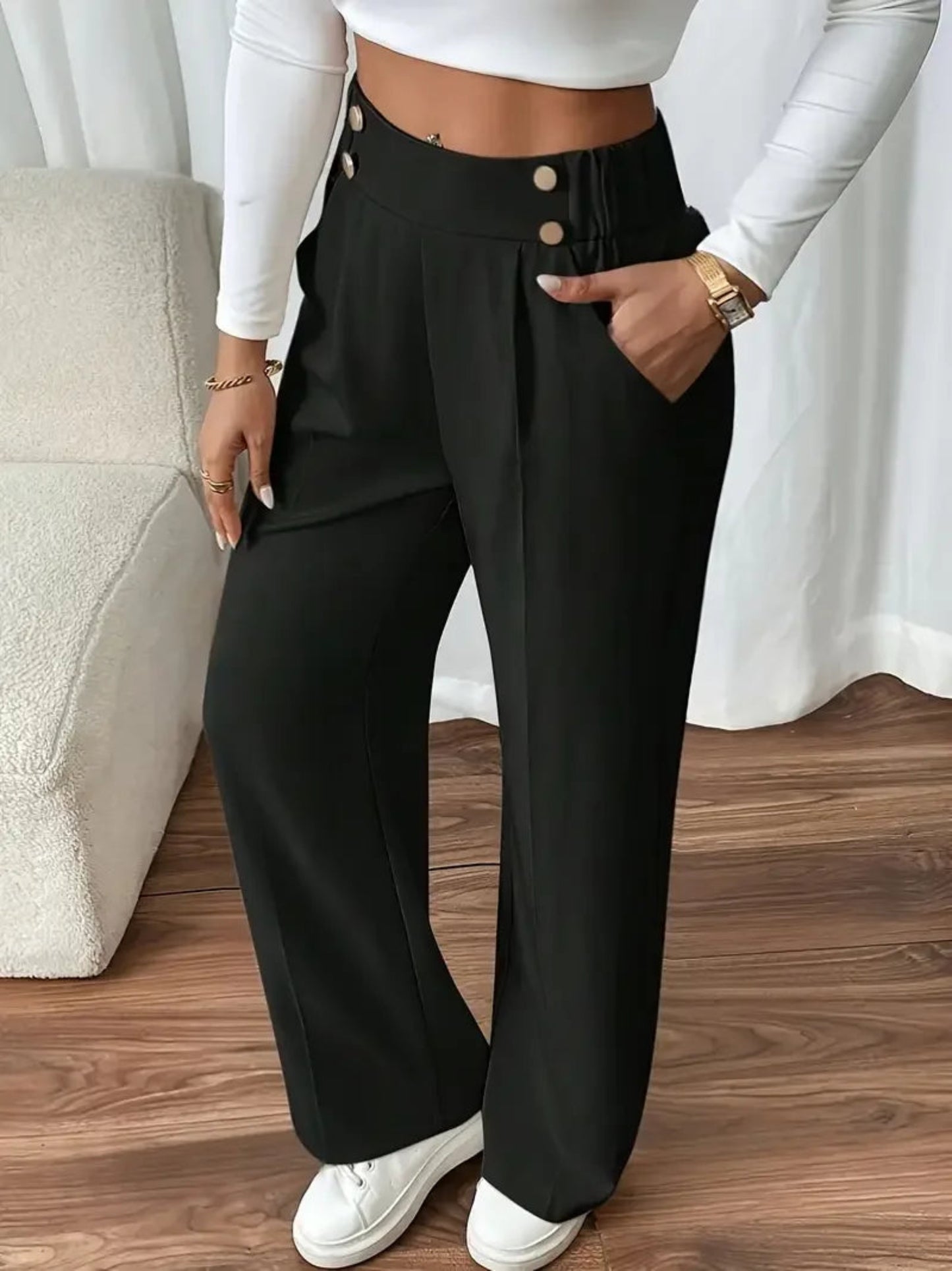 Person wearing black wide-leg pants with a white top and white sneakers on a wooden floor.