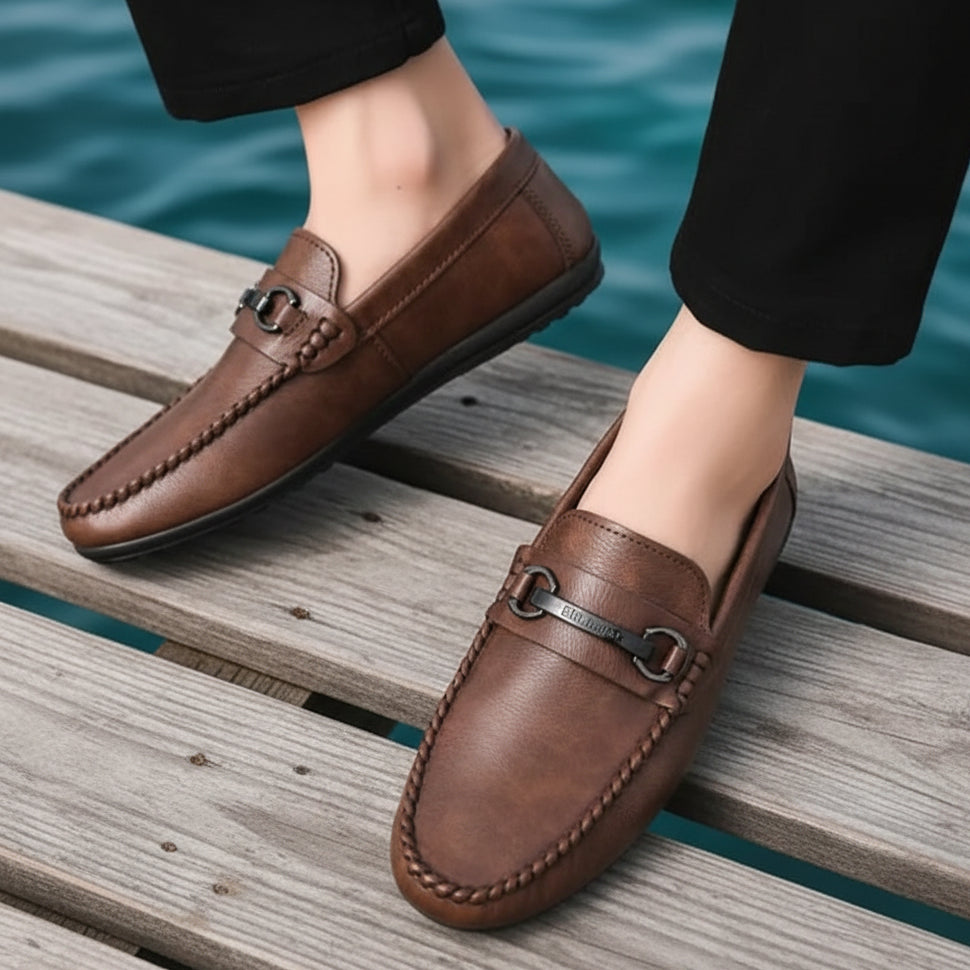 Brown loafers worn with black pants on a textured surface.