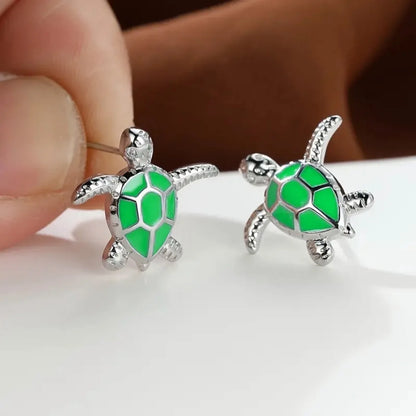 Green turtle-shaped earrings held by a hand on a white surface