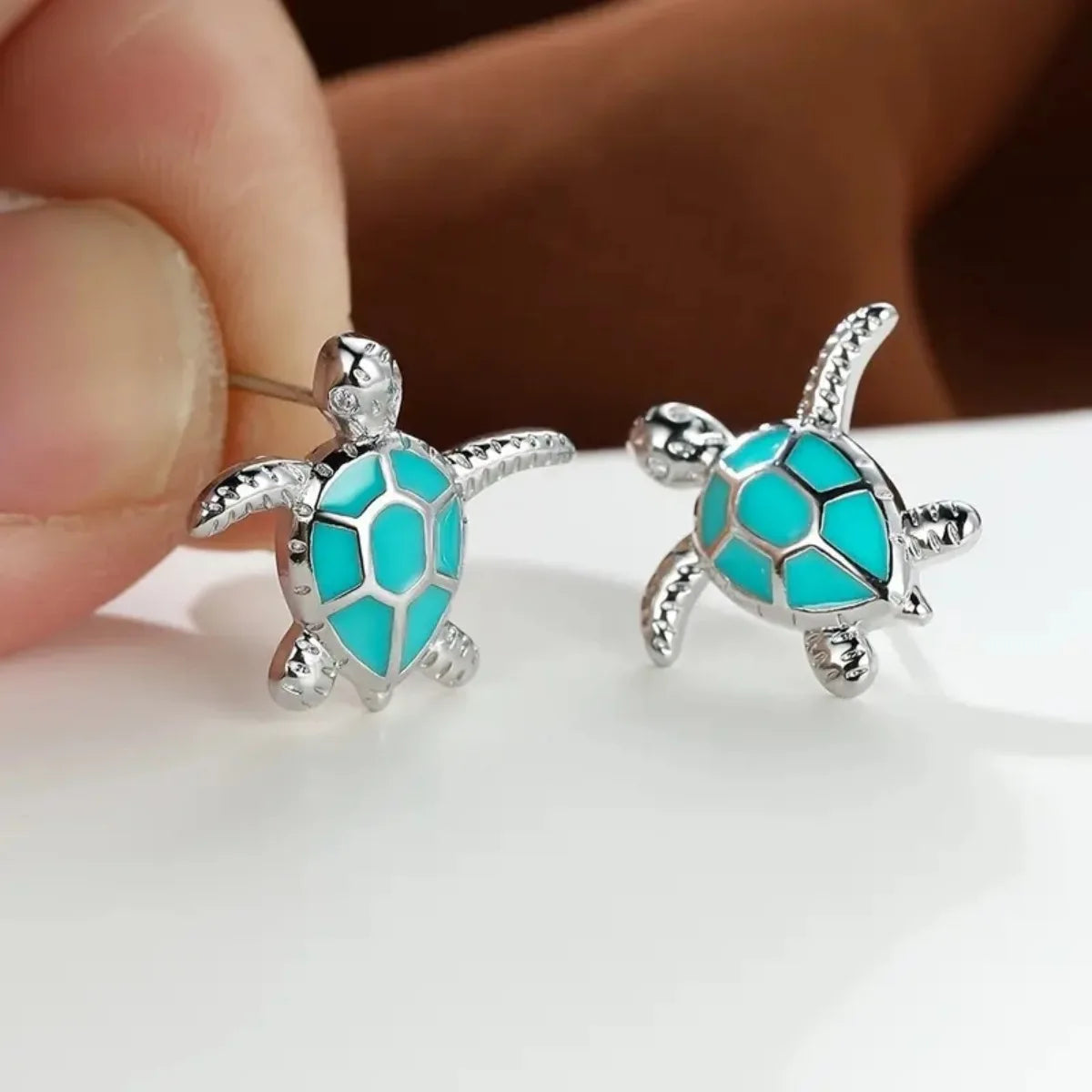 Turquoise turtle earrings held between fingers on a white background