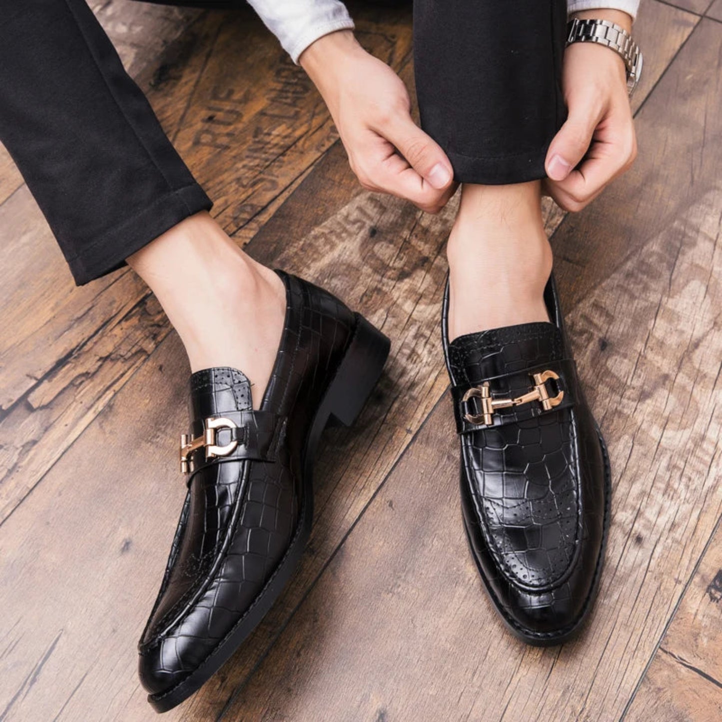Black dress shoes with gold buckles worn on a wooden floor