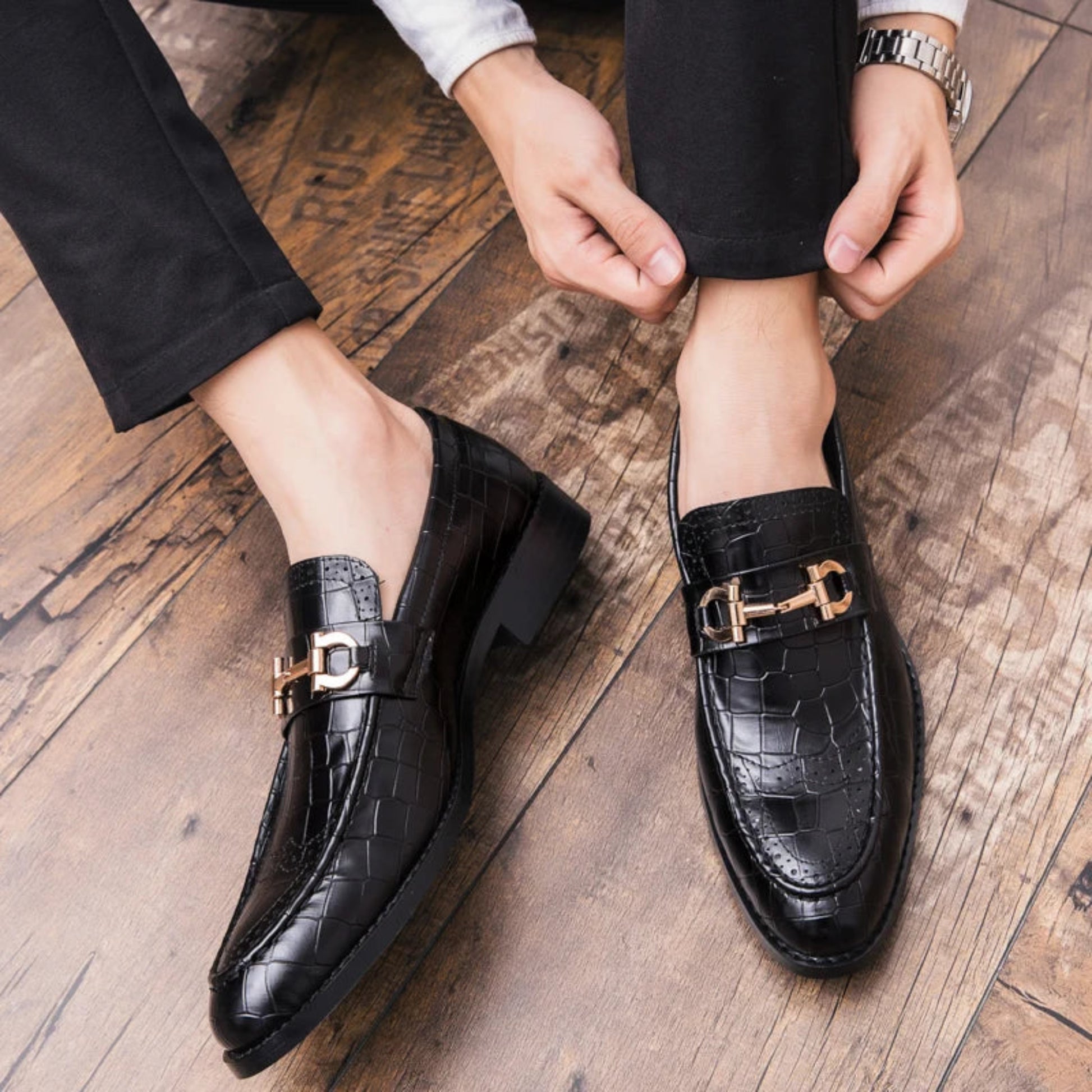 Black dress shoes with gold buckles worn on a wooden floor
