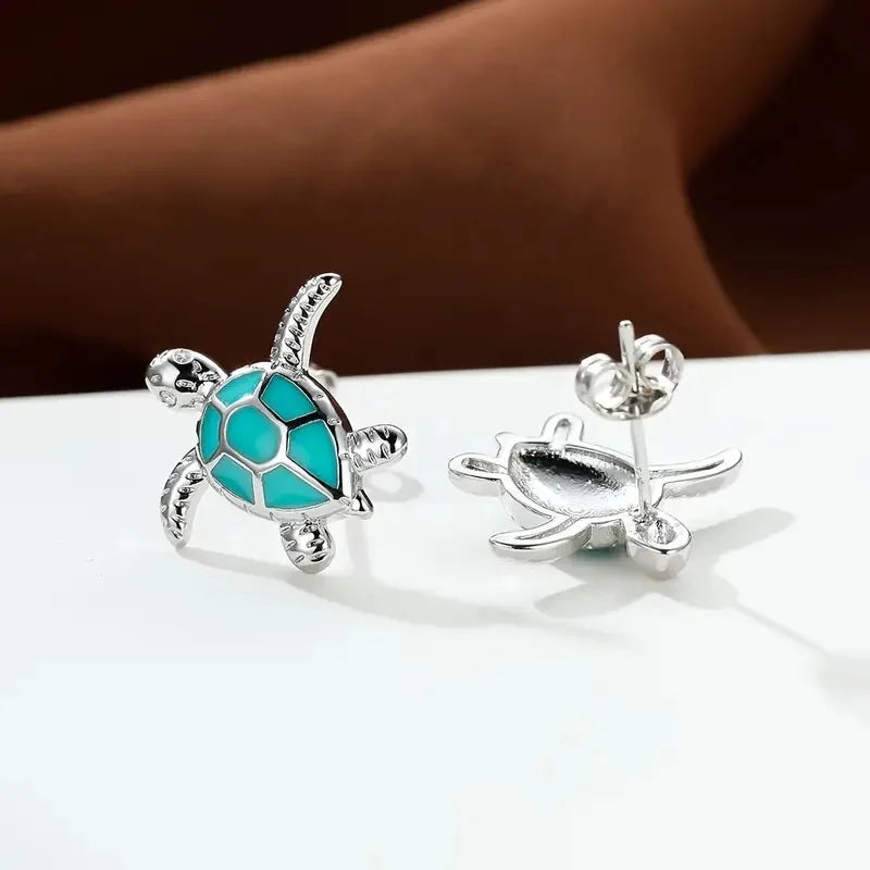 Turtle-shaped earrings with turquoise center and silver accents on a white surface.
