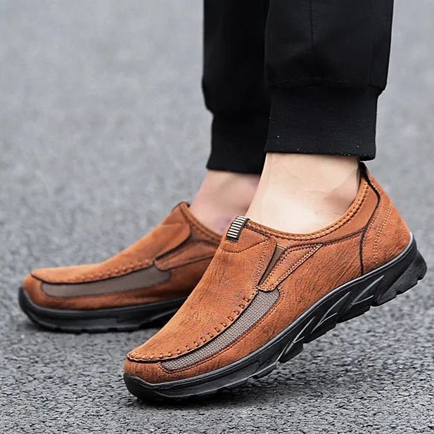 Brown loafers worn with black pants on a gray surface, with text 'Uninhibited New Fashion Sports Shoes' on the right.