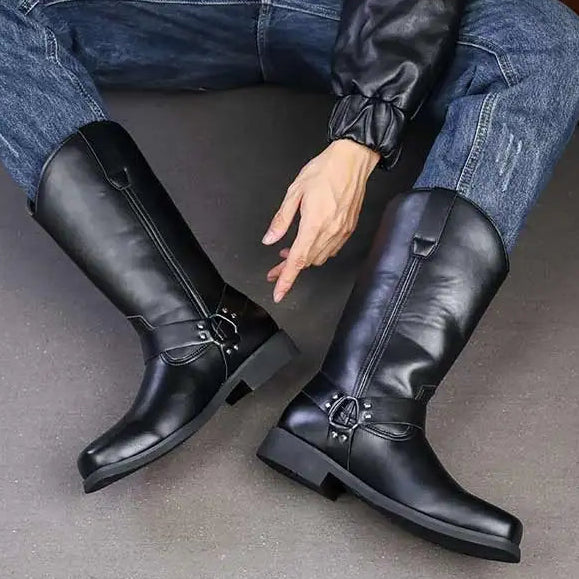 Black knee-high boots worn with blue jeans on a gray floor.
