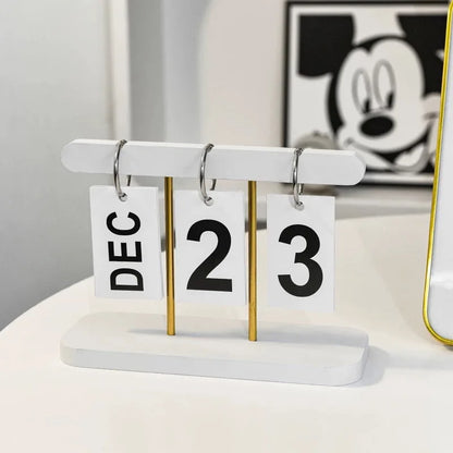 Desk calendar with 'DEC 23' on a white surface, with a blurred Mickey Mouse poster in the background.