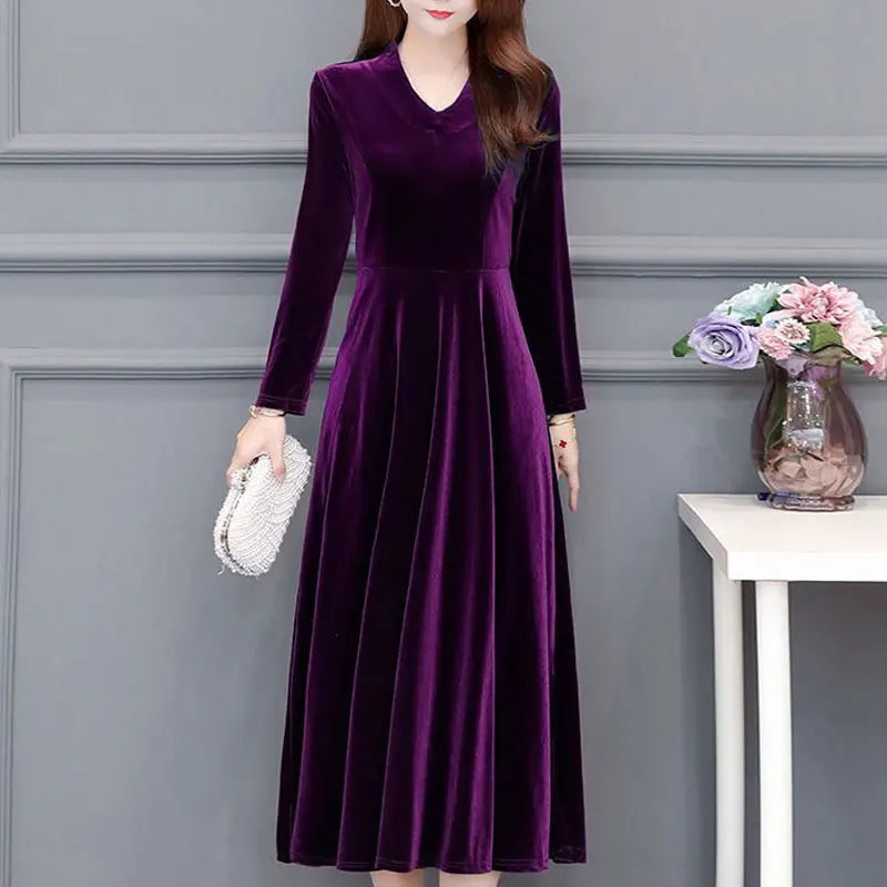 Woman wearing a purple velvet dress against a gray wall with a vase of flowers on a table.