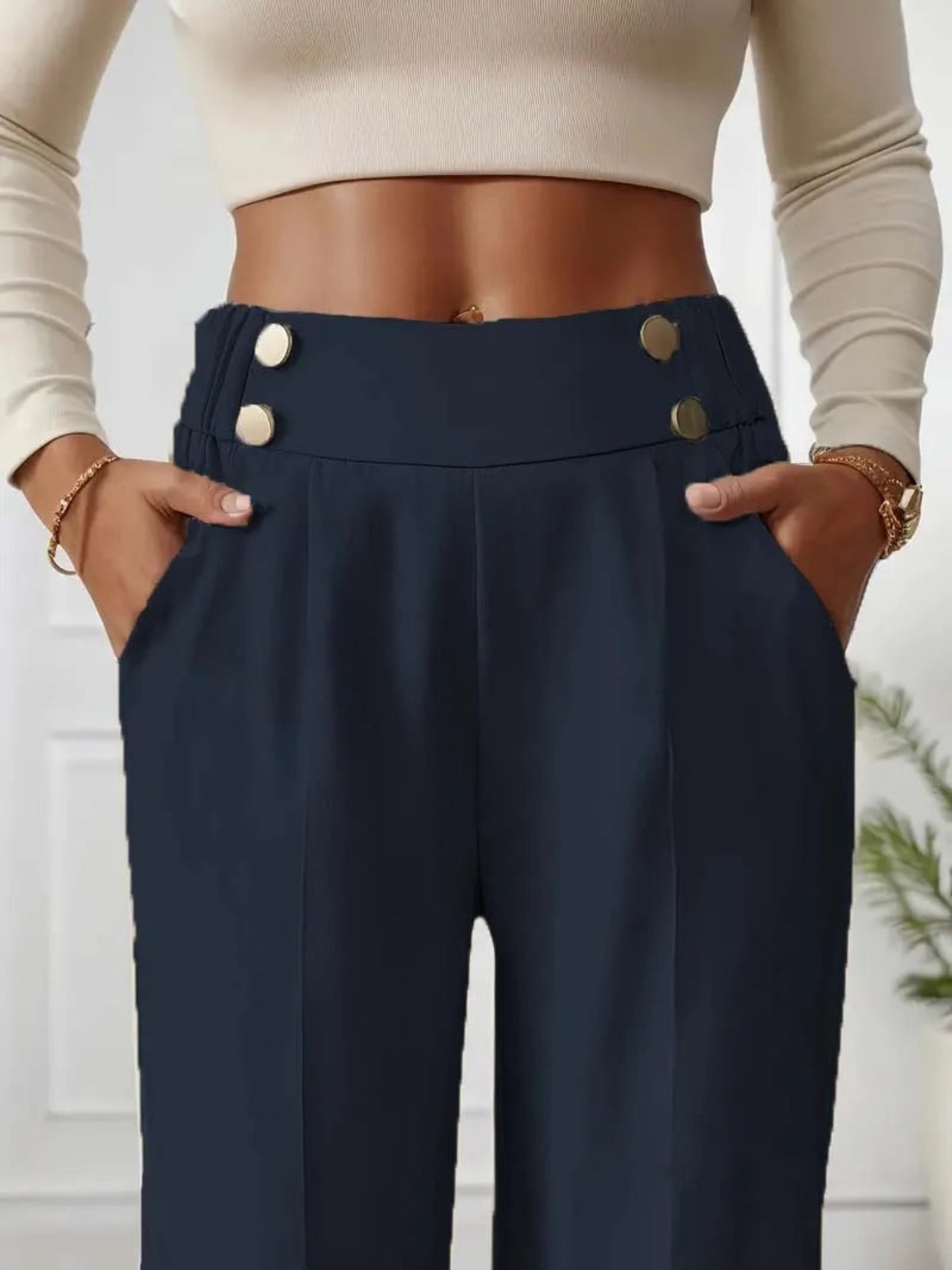 Navy blue pants with button details worn by a person, against a neutral background