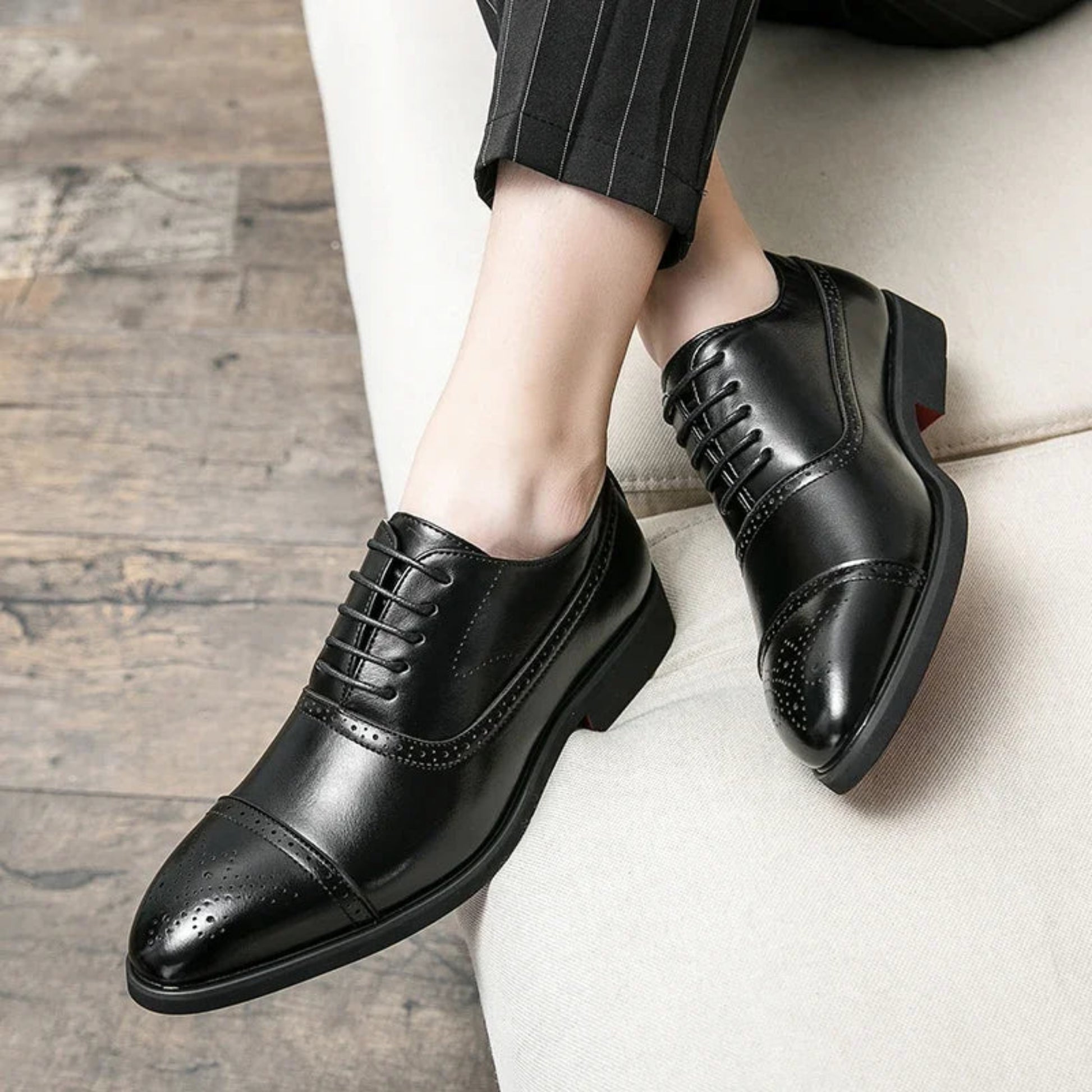 Black dress shoes worn with a suit on a wooden floor.