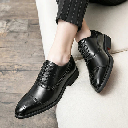 Black dress shoes worn with a suit on a wooden floor.