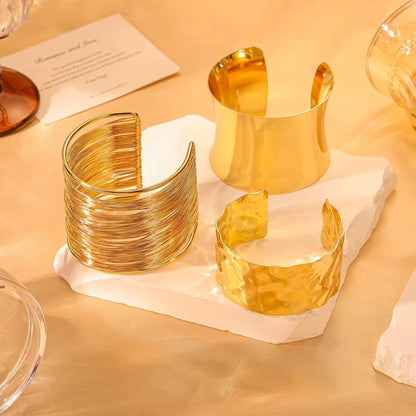 Three gold cuff bracelets on a white stone surface with a warm beige background.