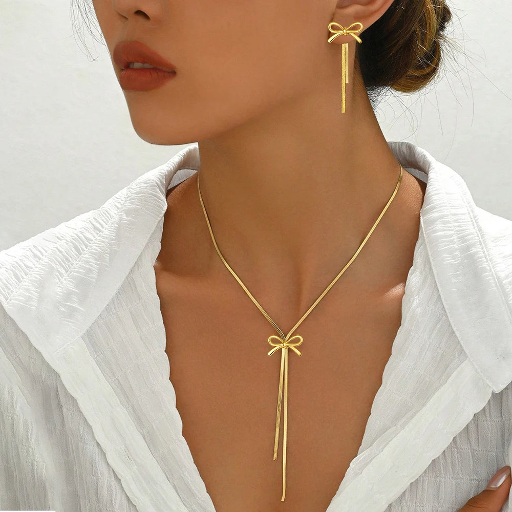 Gold bow-shaped necklace and earrings on a model against a white background