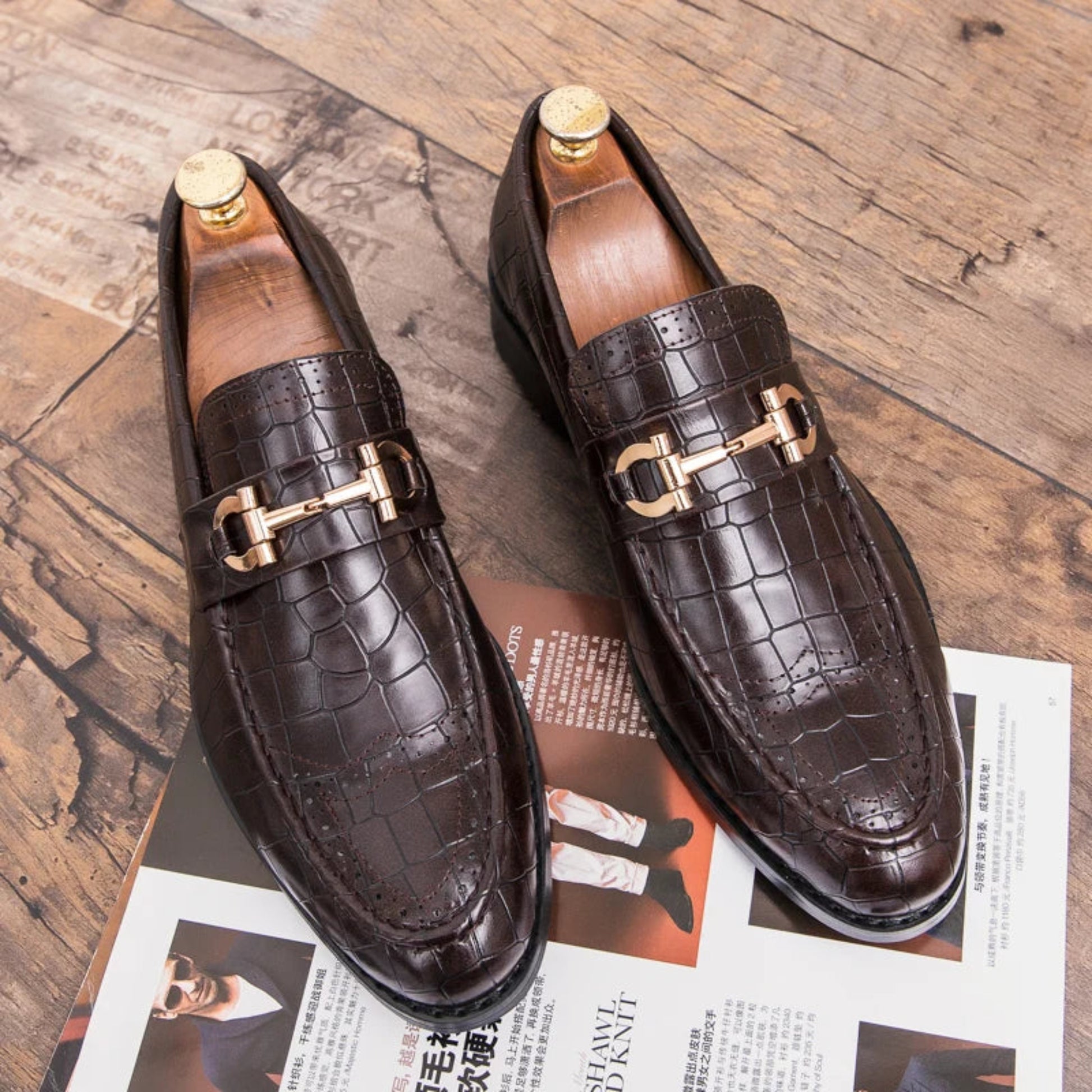 Brown leather loafers with gold buckles on a wooden surface