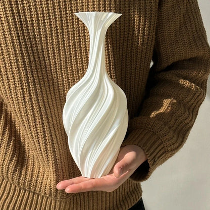 Person holding a white swirled vase against a brown sweater background