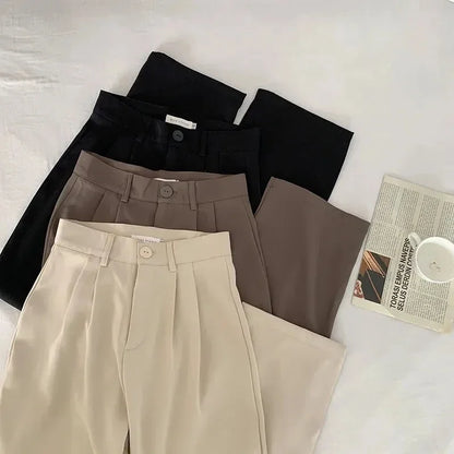 Three pairs of pants in black, brown, and beige on a light surface with a newspaper and cup.