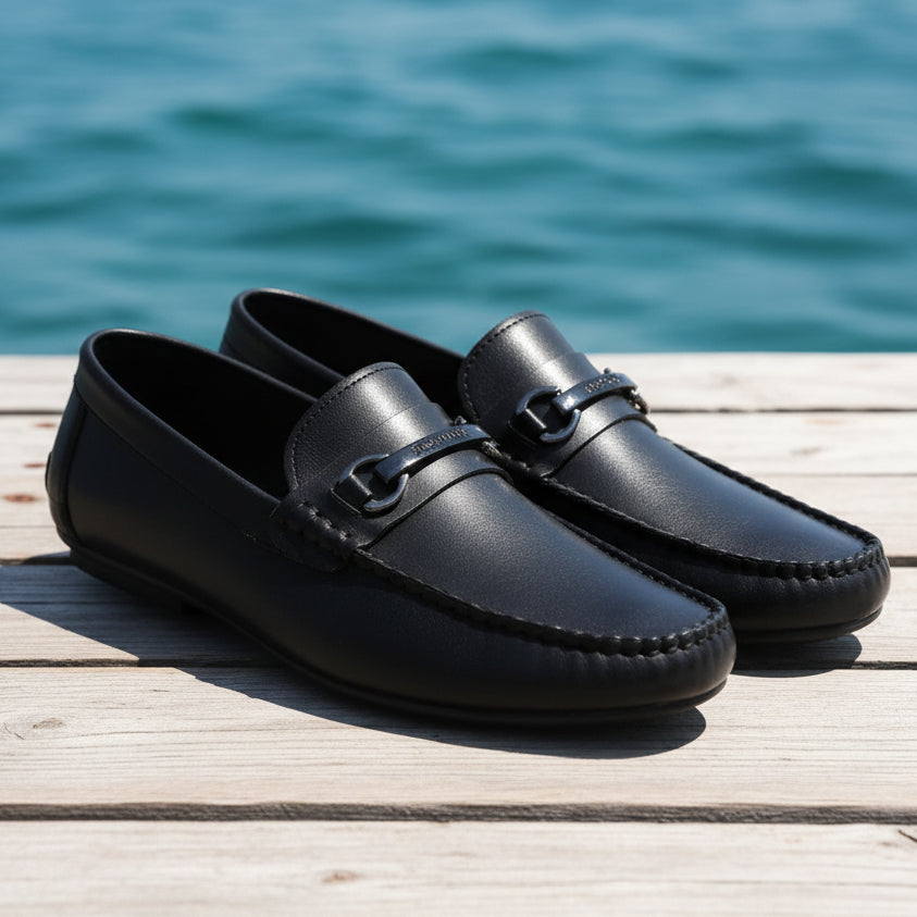 Black leather loafers with a silver buckle on a textured surface
