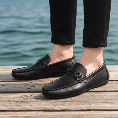 Black leather loafers worn with black pants on a blurred indoor background