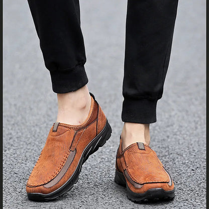 Brown leather shoes worn with black pants on a gray pavement background