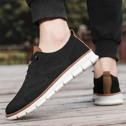 Black knit shoes with white soles worn by a person on a wooden floor.