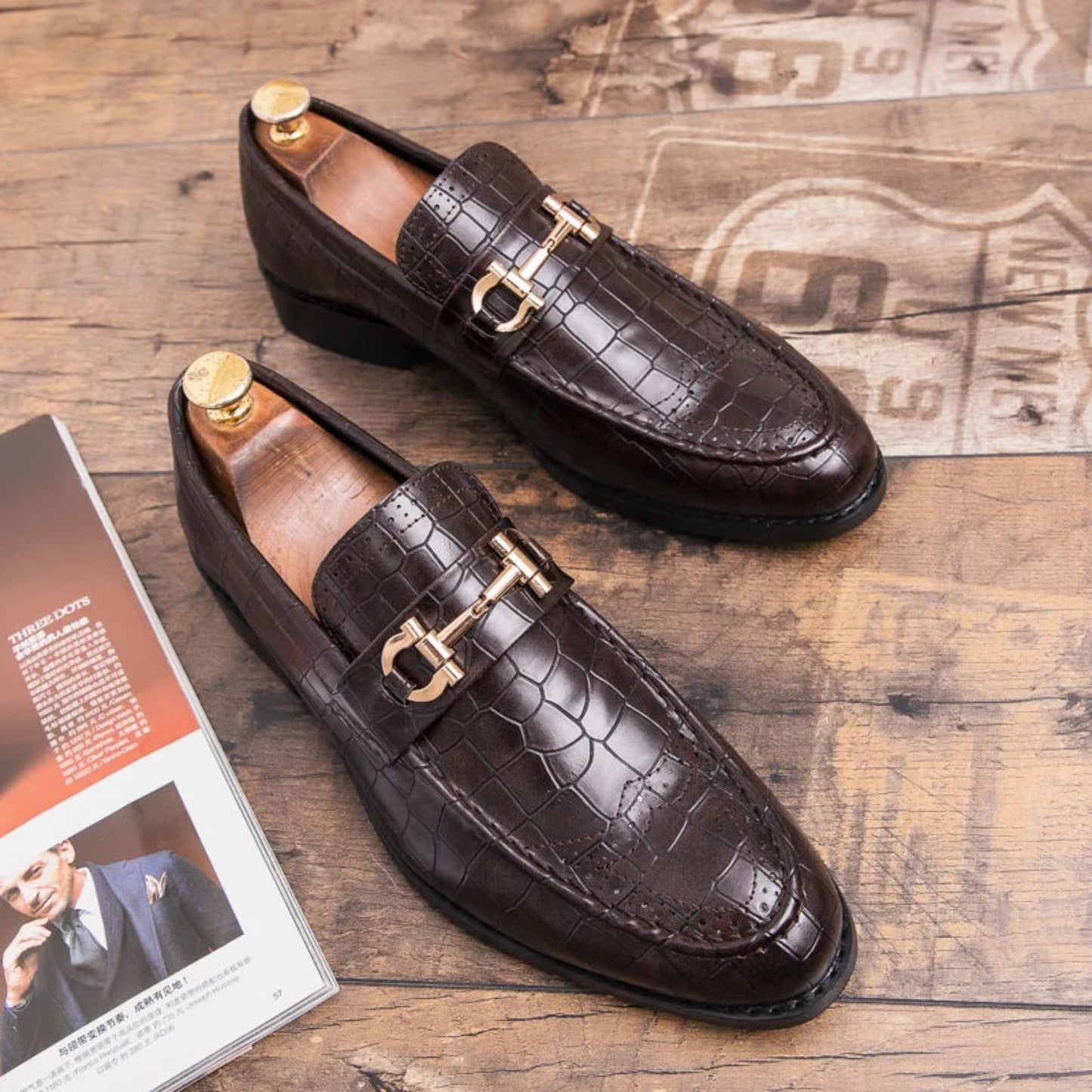 Brown leather loafers with gold buckles on a wooden surface